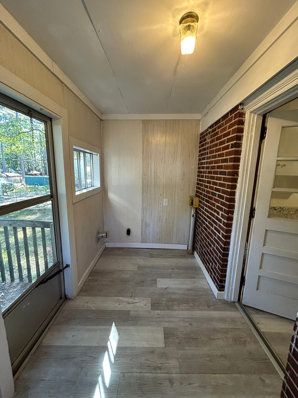 A room with a wooden door and a window with a view of a deck.