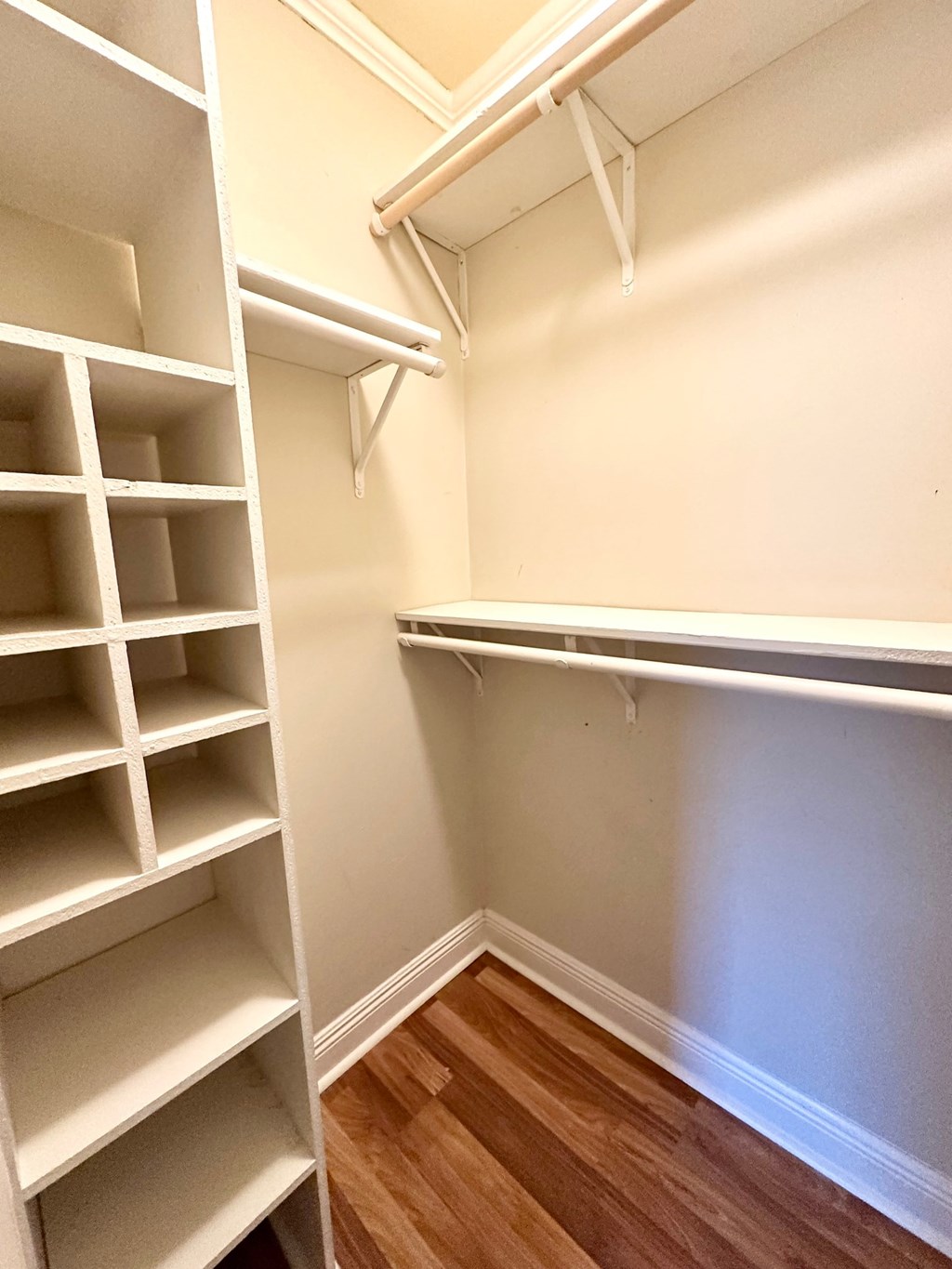 A white shelving unit with multiple compartments is installed in a corner of a room with wooden flooring.
