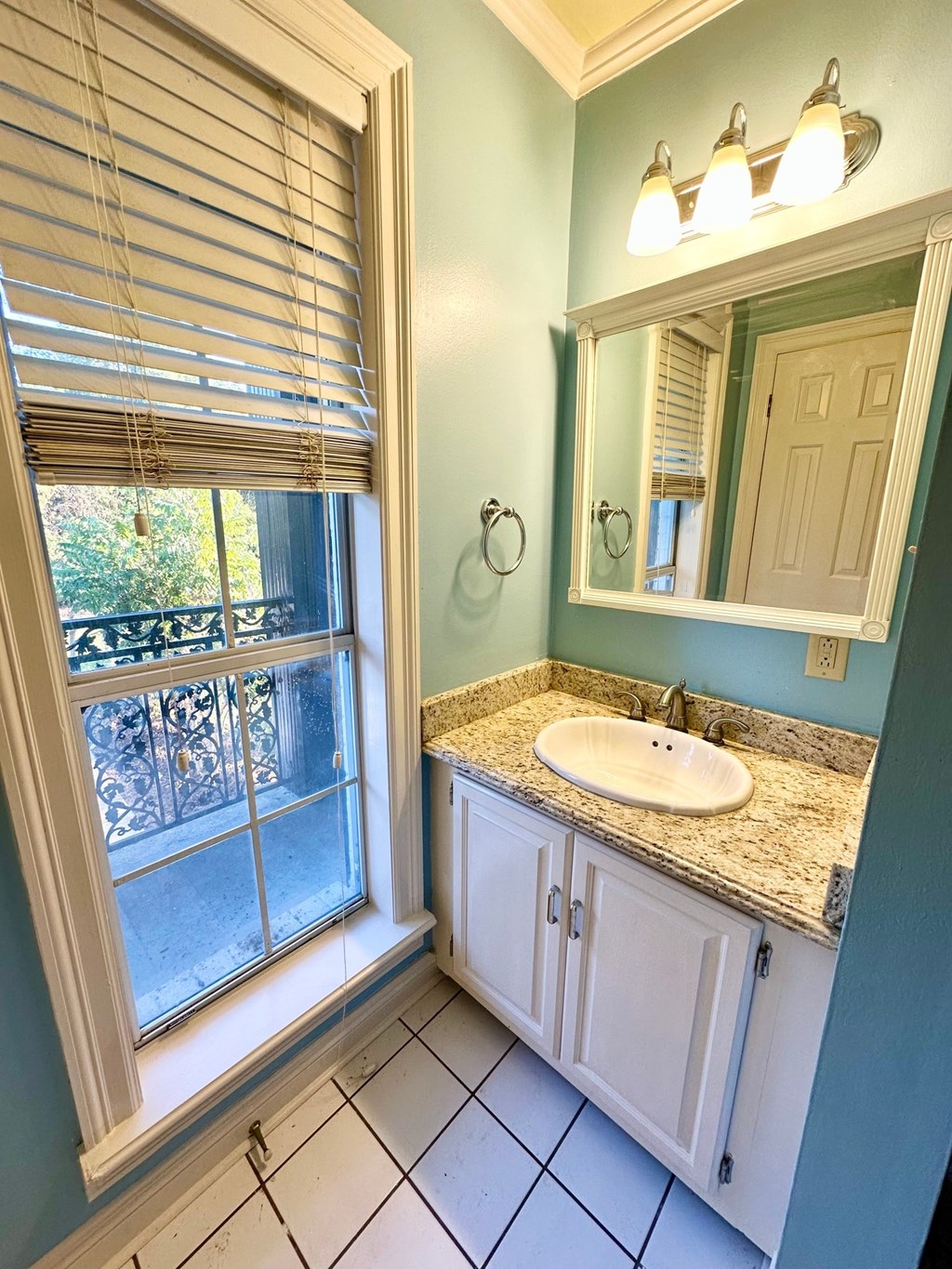A bathroom with a sink, mirror, and window with blinds.