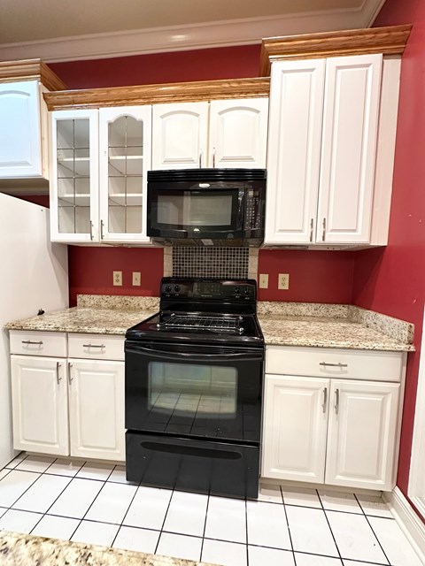 A black stove top oven in a kitchen with white cabinets.