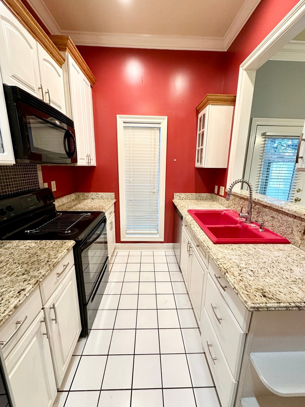 A kitchen with red walls and white cabinets.