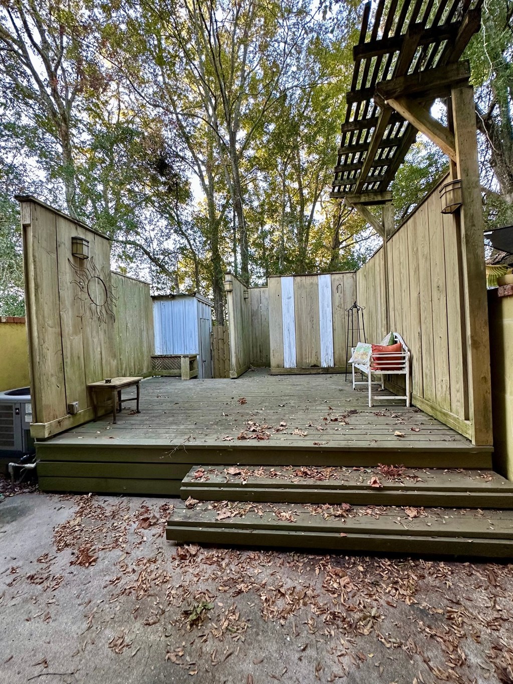 A wooden deck with a bench and a chair is surrounded by trees.