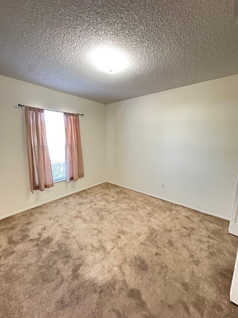 A room with a carpeted floor and a window with curtains.