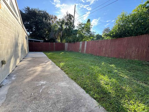 A concrete pathway leads through a backyard with a red fence.