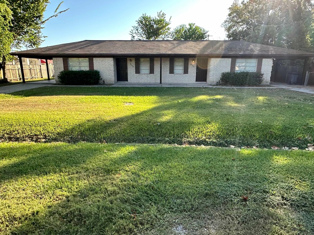 A house with a brown roof and white walls with a green lawn in front.
