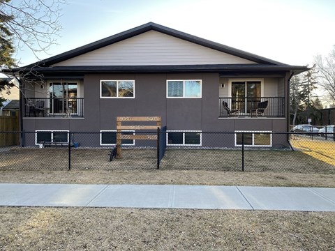 A grey house with a brown bench in front.