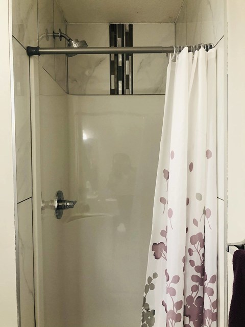 A white shower curtain with purple flowers hangs in a white shower stall.