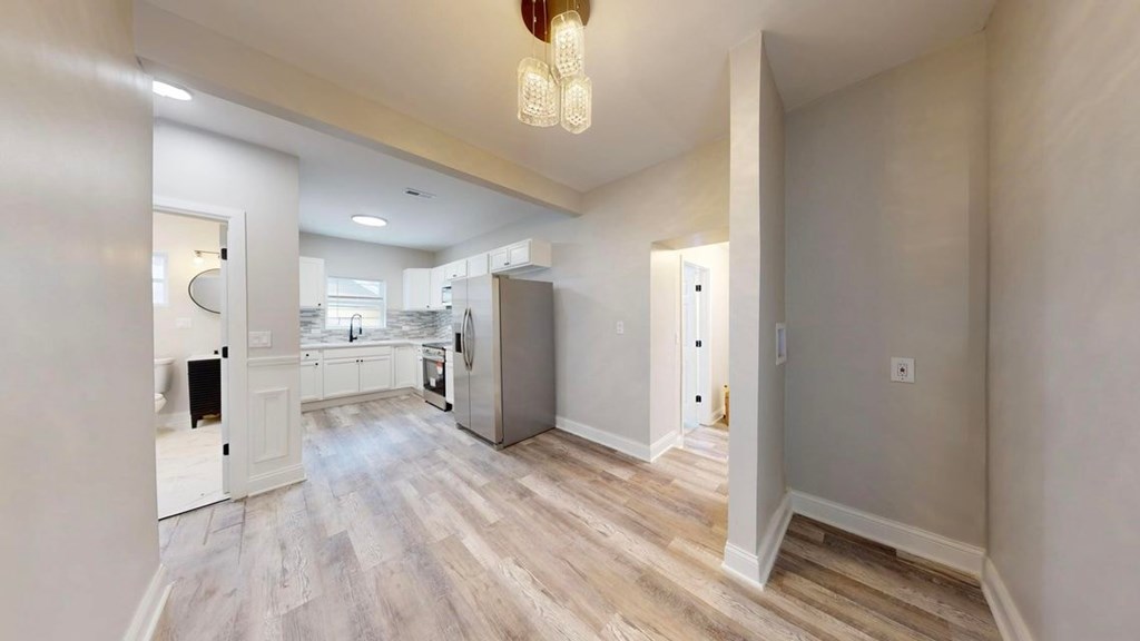 A spacious room with light wood flooring and a chandelier hanging from the ceiling.