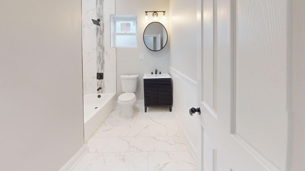 A white bathroom with a toilet, sink, and mirror.