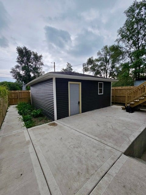 A small blue building with a grey roof and a grey door is surrounded by a concrete patio.