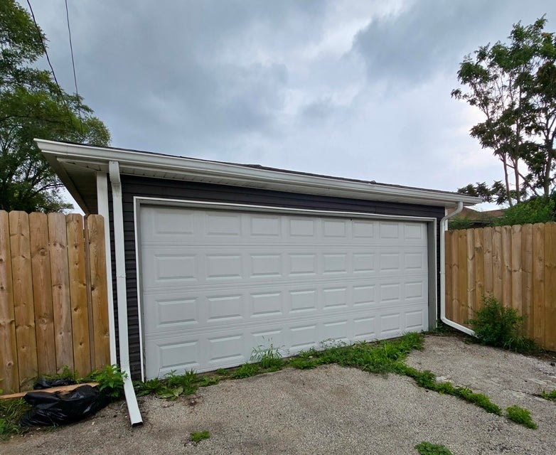 A white garage door is closed and there is a black bag on the ground.