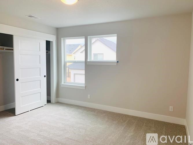 A room with a white door and a window with a view of a house across the way.