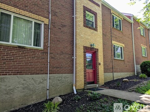 A red door is on the right side of a brick building.
