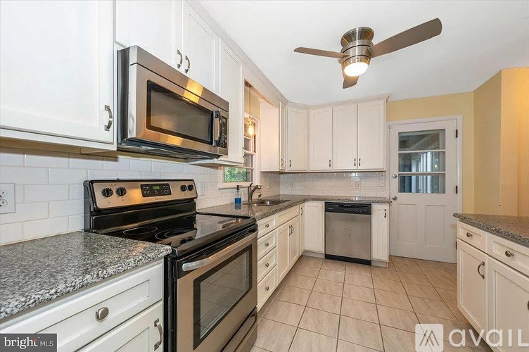 A kitchen with a black microwave above a stove and white cabinets.
