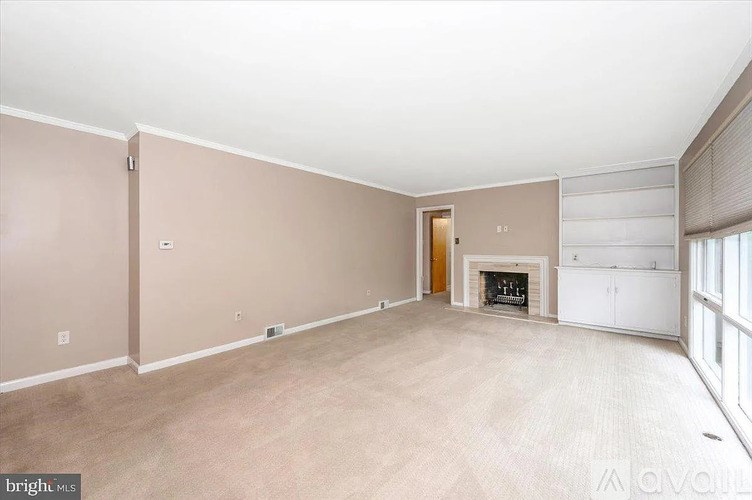 A spacious living room with a fireplace and a door leading to another room.