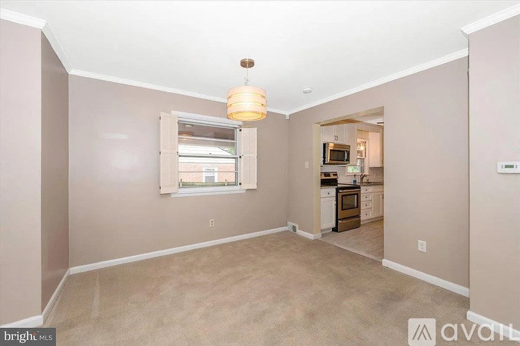 A well-lit, empty room with a window and a kitchenette in the background.