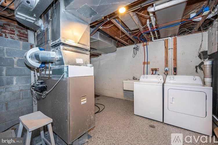 A room with a washer and dryer, a stool, and a wall of pipes and ducts.