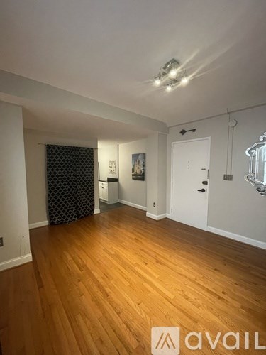 A room with wooden floors and white walls, with a black and white patterned curtain on the window.