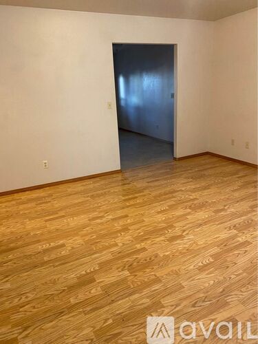 A room with wooden flooring and a doorway leading to another room.