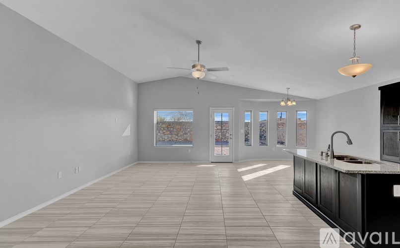 A spacious kitchen and living room with a fan and pendant lights.