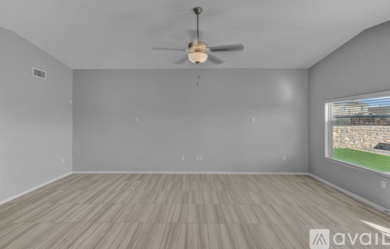 A room with a ceiling fan and a window overlooking a field.