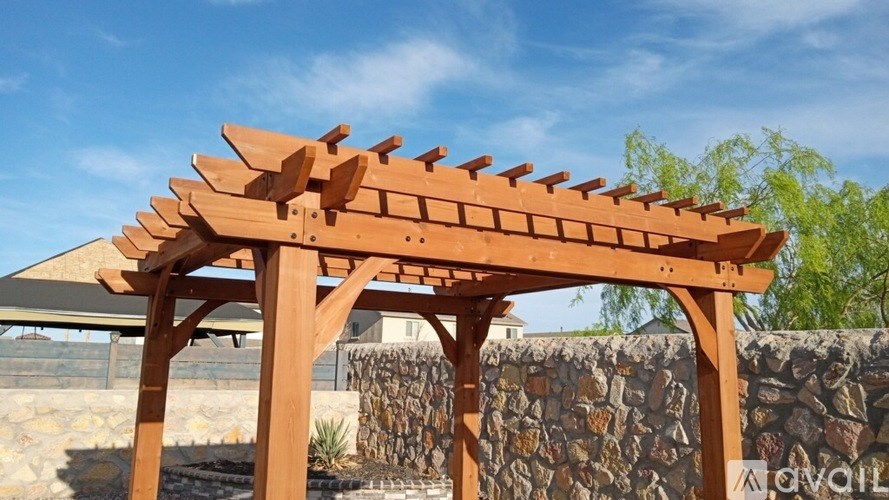 A wooden pergola with a stone wall in the background.