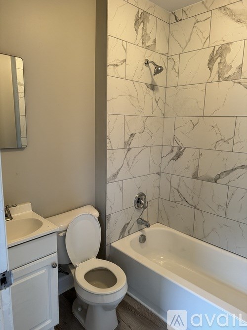 A white toilet sits next to a bathtub in a bathroom with marble tiles.