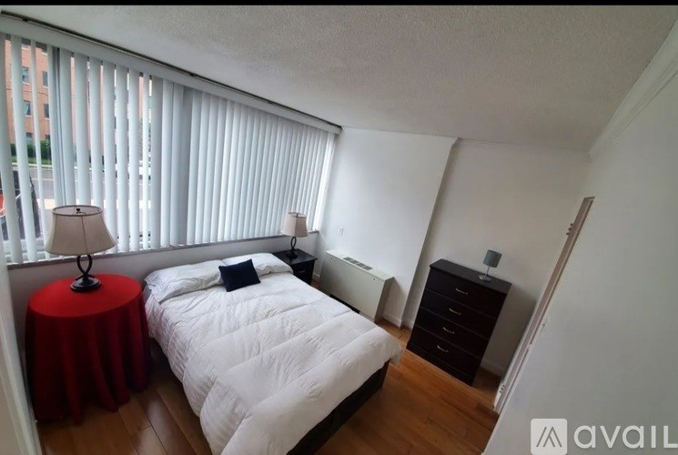 A bedroom with a bed, nightstand, and a window with blinds.