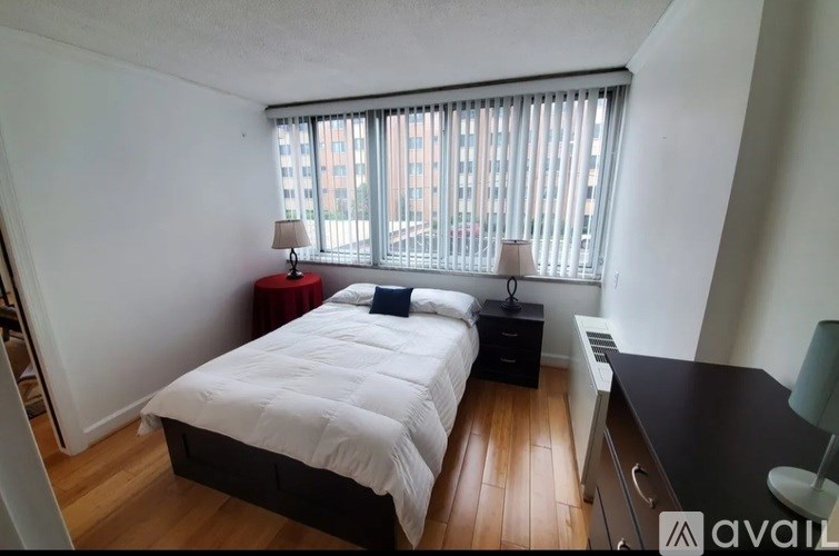 A bedroom with a large bed, a desk, and a window with blinds.