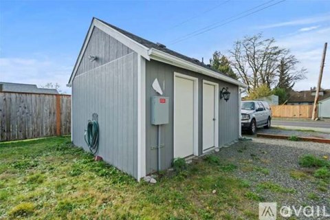 A small grey building with a white door and a green hose on the wall.