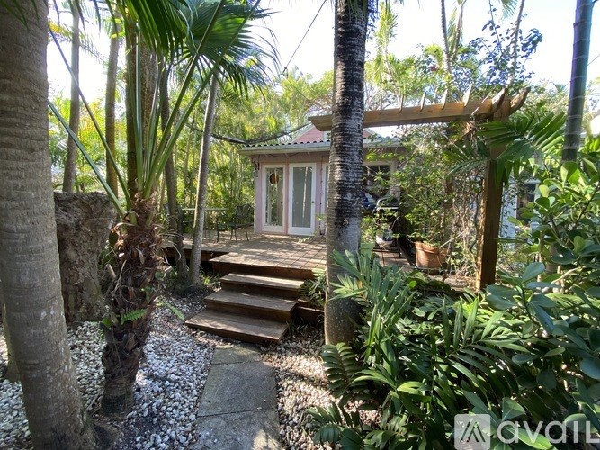 A small white building with a glass door is surrounded by green plants.