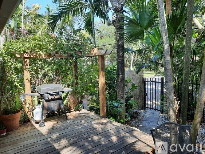A wooden deck with a grill surrounded by green plants.