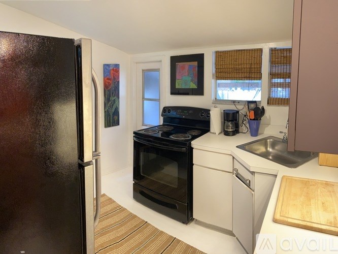 A kitchen with a black fridge, white cabinets, and a black oven.