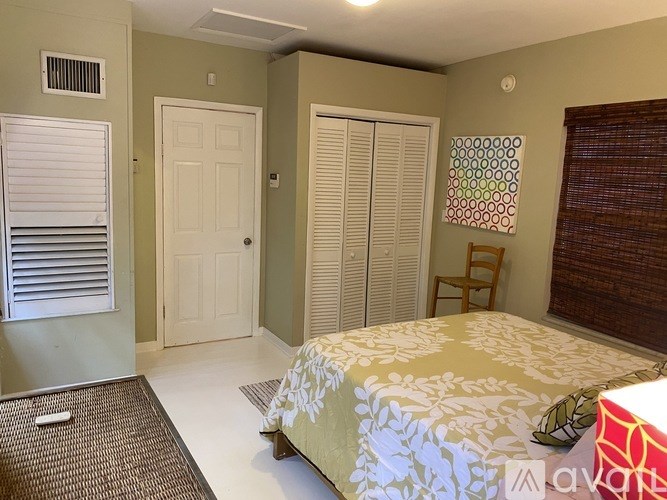 A bedroom with a bed, a chair, and a window with blinds.