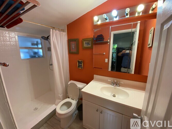 A bathroom with orange walls has a toilet, sink, and shower.