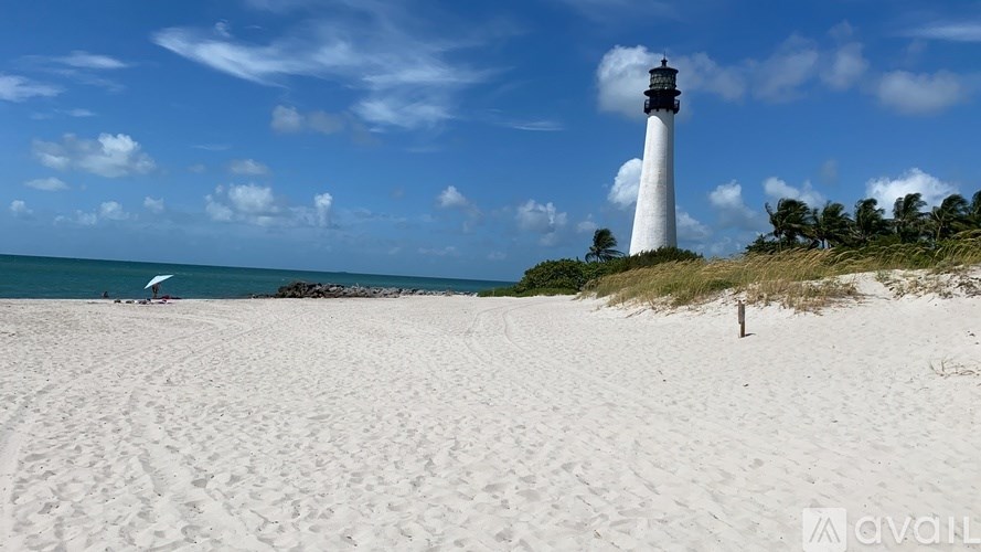 A white lighthouse stands on a sandy beach under a blue sky.