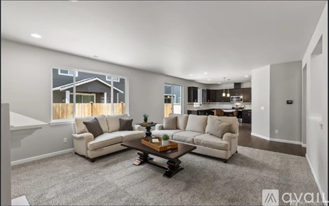 A living room with a grey carpet and a coffee table in the center.