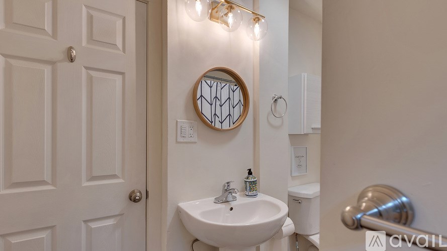 A white bathroom with a round mirror and lights above the sink.