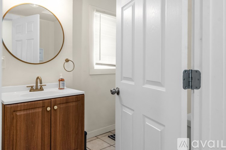 A bathroom with a white door, a round mirror, and a wooden cabinet with a white countertop.