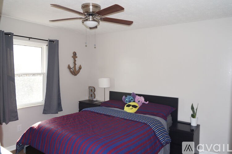 A bedroom with a bed, a ceiling fan, and a window with curtains.