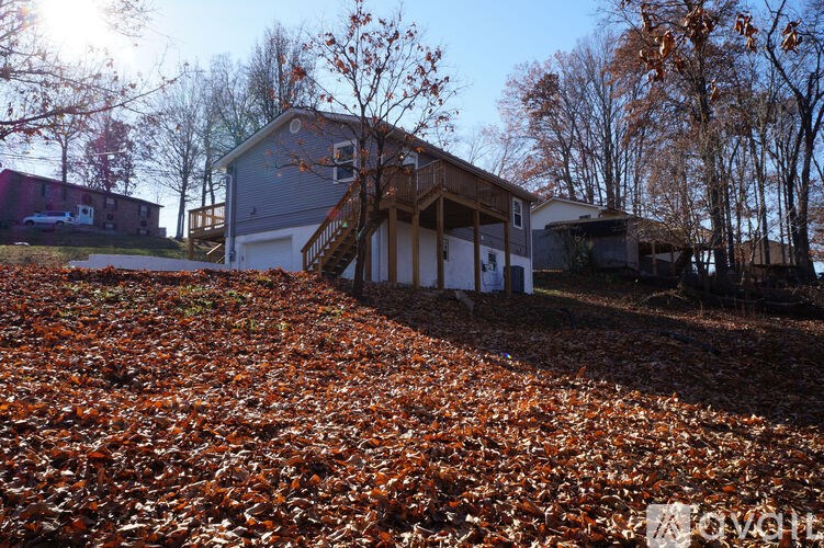 A house with a grey roof and white walls is surrounded by a carpet of orange leaves.