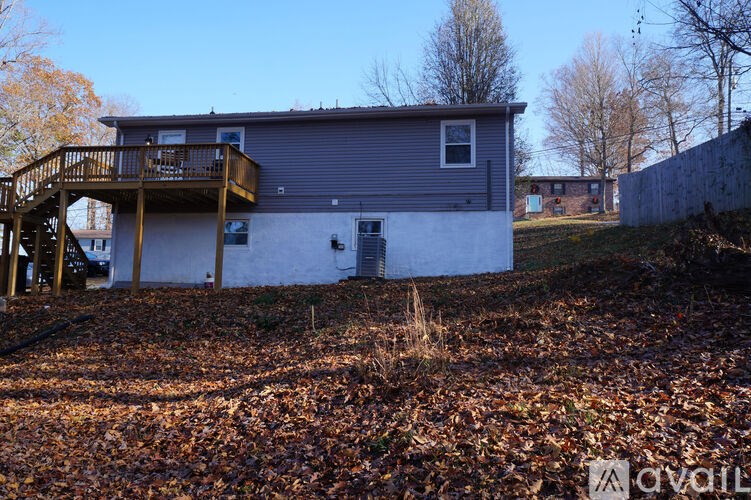 A house with a grey roof and a balcony is surrounded by a field of dry leaves.