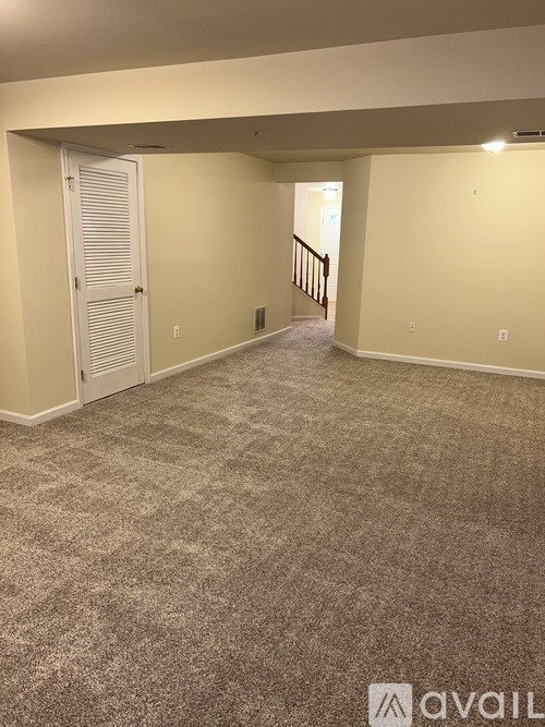A carpeted room with a staircase in the background.