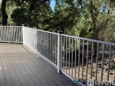 A white railing on a wooden deck with trees in the background.
