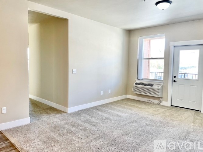 A room with a carpeted floor, a window with blinds, and a door leading to a balcony.