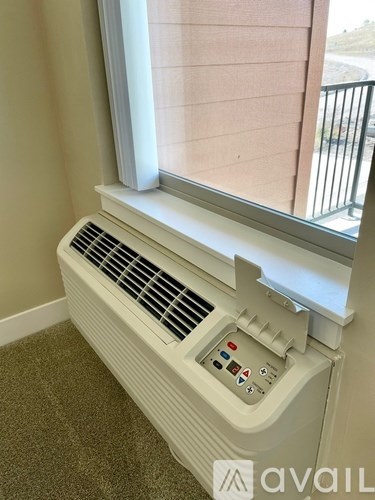 A window air conditioner is sitting on a carpeted floor next to a window.
