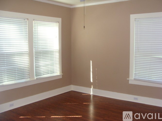 A room with wooden floors and two windows with blinds.