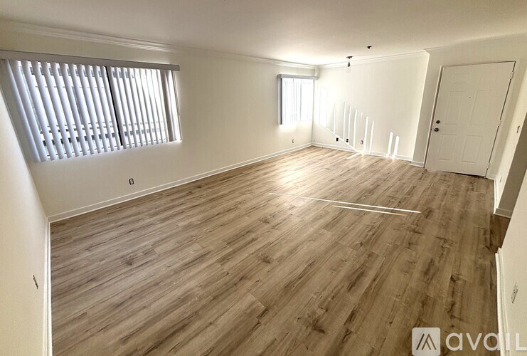 A spacious room with wooden flooring and a window with blinds.