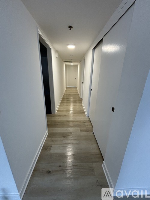 A long, narrow hallway with white walls and wooden flooring.