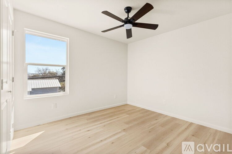 A room with a ceiling fan and a window overlooking a rooftop.